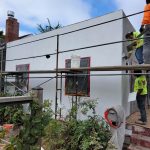 Workers painting a house on a hillside, showcasing teamwork and skill in a picturesque outdoor setting.