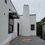A house with a white roof and chimney is being painted, showcasing fresh colors and a vibrant atmosphere.