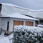 A snow-covered house with a ladder resting on its roof, showcasing a serene winter landscape.