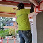 A man in a yellow shirt is painting a ceiling with a roller, focused on his task.
