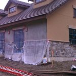 A house under construction, partially covered with a white cloth, showcasing the building process and materials used.