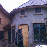A house under construction featuring a large window, showcasing the framework and building materials in progress.