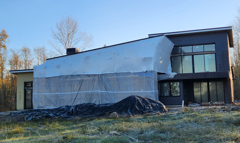 A house under construction, partially covered with a tarp, showcasing the building process and materials used.